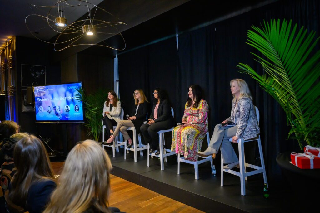 Five women sitting on stools on a small a stage in front of an audience