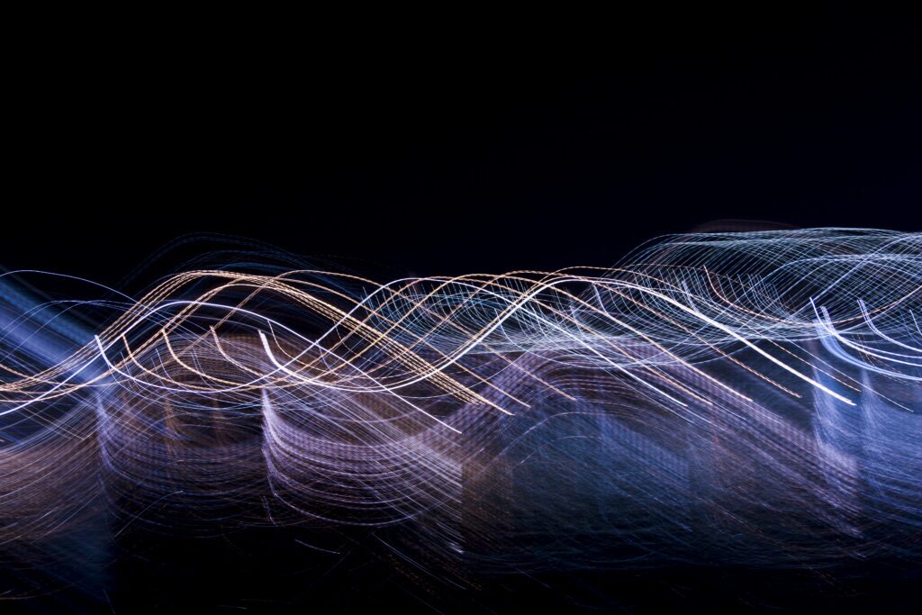 Abstract blue, white, and purple light trails flowing across a dark background, evoking continuous cybersecurity testing, interconnected systems, and the ongoing protection of a digital environment.